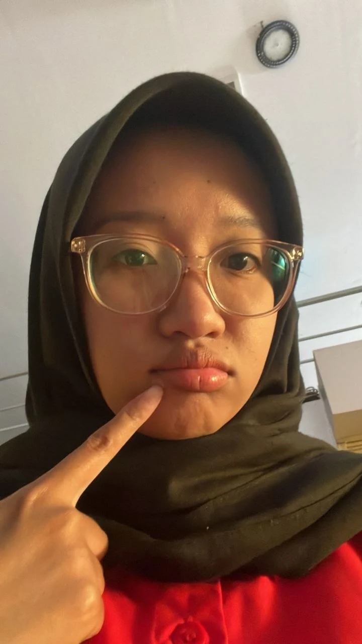 Caca in a dark hijab and red shirt, making a playful face