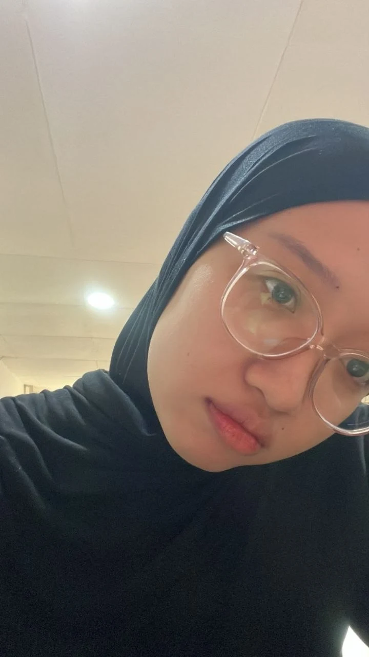 Caca wearing a black hijab, leaning toward the camera with her head tilted