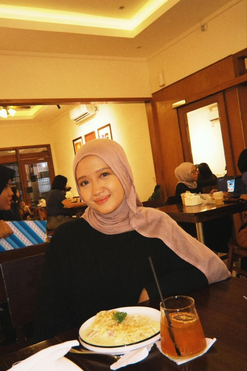 Caca smiling at a cafe table with a meal and an iced drink